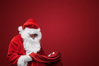 Noel Baba klasik kırmızı elbisesiyle, kendine güvenen bir çanta tutuyor.