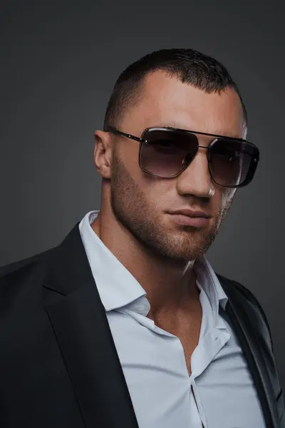 A close-up portrait of a well-groomed man in sunglasses, dressed in an elegant, high-end classic suit with a white shirt