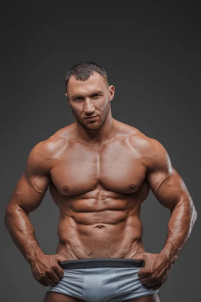 白いブリーフを身に着け 灰色の背景に彼の裸の筋肉の胴体を展示する よく整えられたモデルの外観を持つ頑丈な男の肖像画 — ストック写真