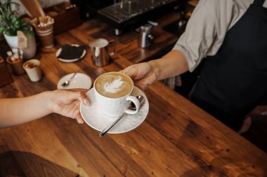 Kahveci, ahşap kafe tezgahındaki müşteriye kahve resimli güzel bir kapuçino verir.