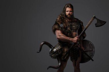 Kürk ve hafif zırh takmış, balta ve kalkan taşıyan, gri arka planda duran korkusuz bir Viking savaşçısı.
