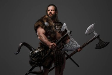 Kürk ve hafif zırhlı vahşi sakallı bir Viking savaşçısı, kemerine bağlı bir miğfer, gri arka planda büyük iki elli bir balta tutuyor.