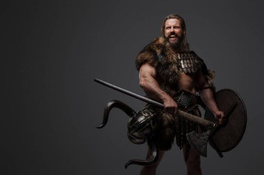 Kürk ve hafif zırh takmış, balta ve kalkan taşıyan, gri arka planda duran korkusuz bir Viking savaşçısı.