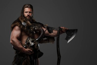 Kürk ve hafif zırhlı vahşi sakallı bir Viking savaşçısı, kemerine bağlı bir miğfer, gri arka planda büyük iki elli bir balta tutuyor.