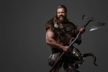 Sert, sakallı, kürk ve hafif zırhlı Viking savaşçısı, elinde büyük iki elli bir balta, gri bir arka plana karşı bağırıyor.
