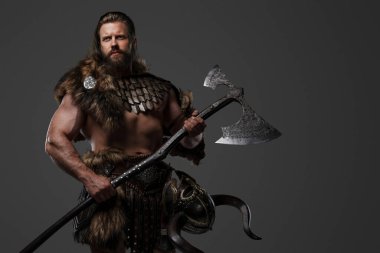 Kürk ve hafif zırhlı vahşi sakallı bir Viking savaşçısı, kemerine bağlı bir miğfer, gri arka planda büyük iki elli bir balta tutuyor.