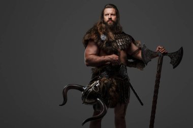 Kürk ve hafif zırhlı vahşi sakallı bir Viking savaşçısı, kemerine bağlı bir miğfer, gri arka planda büyük iki elli bir balta tutuyor.