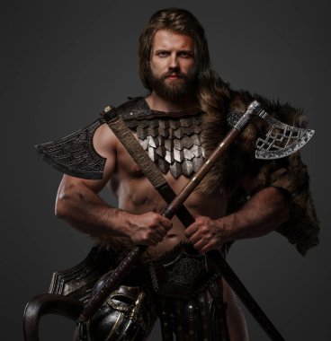 Kürk ve hafif zırh giymiş, kemerine kask takmış ve gri arka planda iki balta tutan haşin sakallı bir Viking savaşçısı.