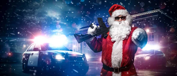 Santa Claus, holding a machine gun, points his finger somewhere, posing in front of police cars with numerous police lights and sirens, amid a snowy stormy night on the street