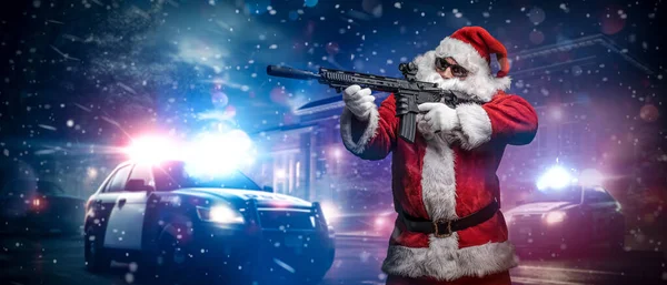 A man dressed as Santa Claus, aiming with a machine gun, poses in front of police cars with numerous police lights and sirens, amid a snowy stormy night on the street