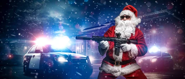 A man dressed as Santa Claus, aiming with a machine gun, poses in front of police cars with numerous police lights and sirens, amid a snowy stormy night on the street