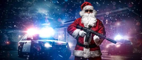 一个人穿着圣诞老人的衣服 拿着机关枪 在街上的雪夜里 在警车前摆姿势 摆出无数警灯和警笛 — 图库照片