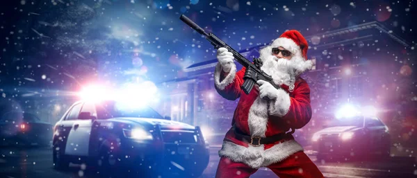 A man dressed as Santa Claus, holding a machine gun, poses in front of police cars with numerous police lights and sirens, amid a snowy stormy night on the street