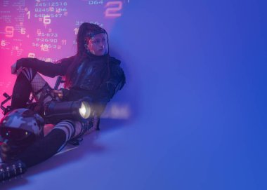 Fütüristik taktiksel siyah takım elbiseli bir kadın motosiklet kaskı ve büyük bir projektörle yerde yatıyor.