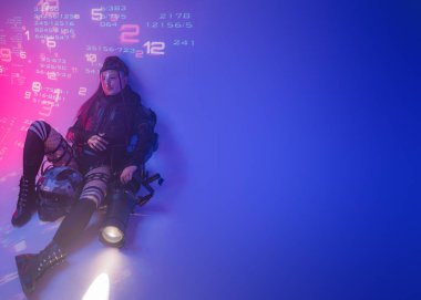 Fütüristik taktiksel siyah bir elbise giymiş bir kadın figürü, projeksiyonlu dijital sembollerden oluşan bir zemin üzerinde büyük bir projektörle yatar.