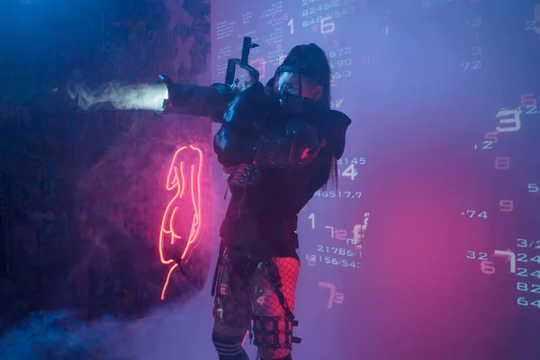 一个身穿未来战术黑色西装的女人拿着一个类似轻炮的大型投影机 站在投射数字符号的背景下 — 图库照片