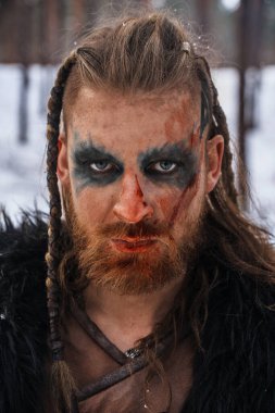 Ayrıntılı savaş boyası ve odaklanmış bakışları olan bir Viking savaşçısının portresi, karlı bir zemin üzerine kurulmuş.