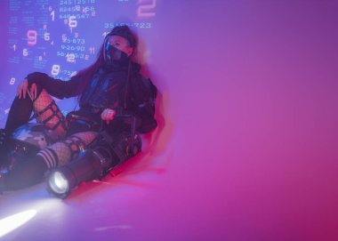 Fütüristik taktiksel siyah takım elbiseli bir kadın motosiklet kaskı ve büyük bir projektörle yerde yatıyor.