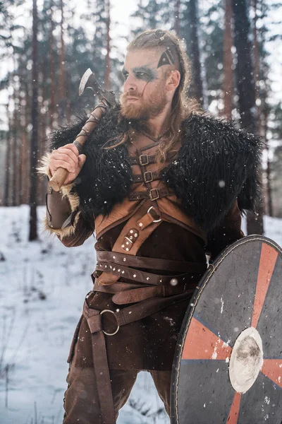 強さと歴史的な北欧の文化を描いた雪の松の森に斧と盾で包まれた激しいヴァイキングの戦士 — ストック写真