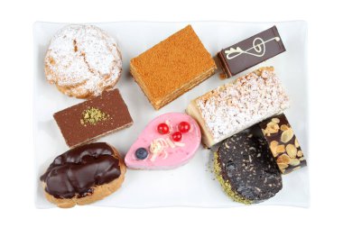 Beyaz bir tabakta eklentiler, tartlar ve krema dolu ikramlar da dahil olmak üzere çeşitli lezzetli hamur işleri ve pastalar sergileniyor..