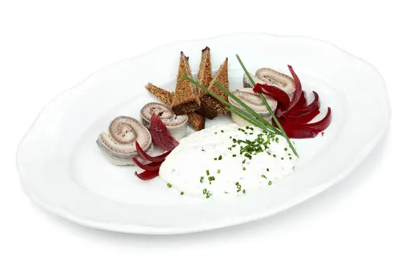 stock image A gourmet dish featuring herring, beetroot slices, and cottage cheese, artistically presented with herbs and toast on a white plate.