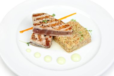 Yanında garnitür ve sosla birlikte beyaz bir tabakta sanatsal olarak servis edilen ızgara et..