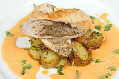 Dilimlenmiş tavuk dolması, kızarmış patates ve yeşil garnitürlü beyaz tabakta kremalı sos.