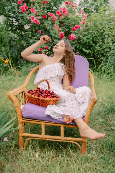 美しい十代の少女が庭の椅子に座ってチェリーを食べる — ストック写真
