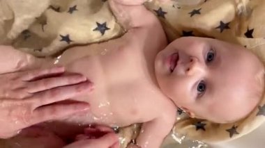 Anne, 3 aylık oğlunu bebek banyosunda yıkıyor. Sevimli küçük erkek bebek dil gösteriyor. Yeni doğan bebek bakımı konsepti. Dikey video.