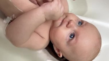 Anne, 3 aylık oğlunu bebek banyosunda yıkıyor, annesi de sıcak suyla yıkıyor. Çocuk gülüyor ve anneme bakıyor. Yeni doğan bebek bakımı konsepti. Dikey video.