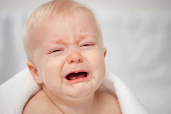 Cute crying baby with closed eyes. Little sad boy - close-up portrait. Child screaming covered by bath towel.