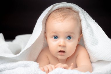 Mavi gözlü şirin bir bebek, yakın plan portresi. Küçük çocuk kameraya bakıyor. Çocuk banyo havlusuyla kaplı olarak yatakta yatıyor..