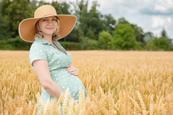 在麦田或大麦地里戴着帽子的快乐孕妇的画像 准妈妈在大自然中悠闲地等待着 用手抚摸着她的肚子 — 图库照片
