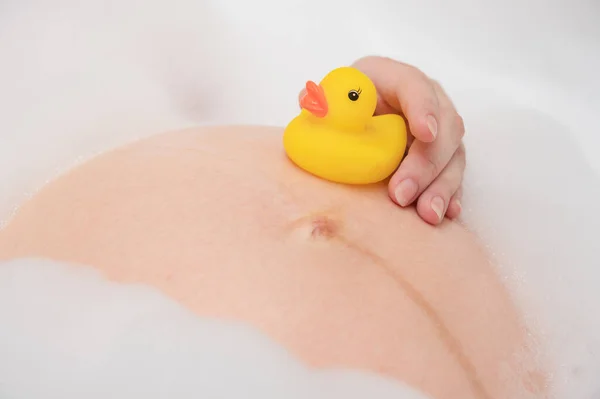 黄色のアヒルのおもちゃで妊娠中の腹 クローズアップ バブルバスを持っている妊婦 ストック画像