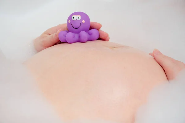 怀孕的腹部与紫罗兰章鱼玩具 正在泡澡的孕妇 免版税图库图片