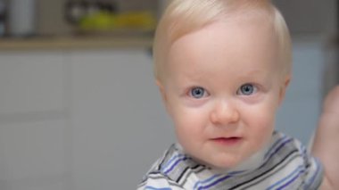 Anne oğlunu kaşıkla bebek mamasıyla besliyor. Çocuk yüksek sandalyede oturarak yulaf lapası yiyor. Annem mutfakta meyveli püreyi besler..