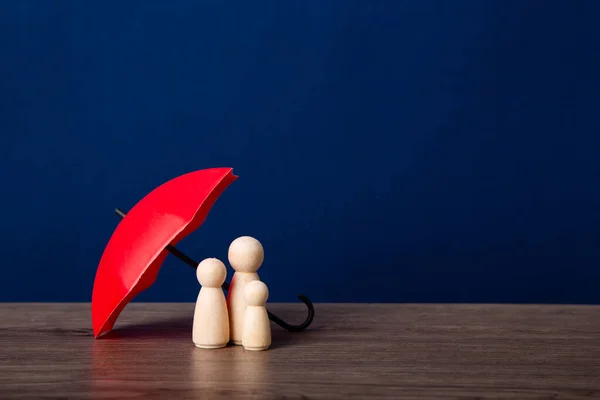 Umbrella and wooden doll figures. Insurance coverage concept.