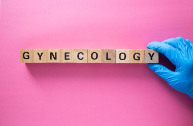 Mavi eldivenli doktor pembe arka planda tahta küpleri kullanarak jinekoloji kelimesini yazıyor.