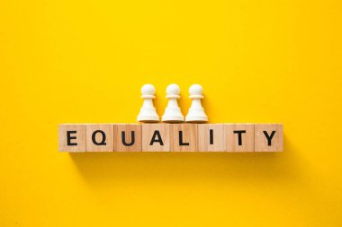 Tahta küplerin üzerinde duran üç beyaz piyon sarı arka planda eşitlik.