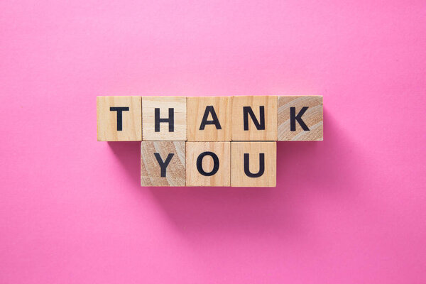 Wooden cubes spelling thank you on a pink background create a simple yet powerful message of gratitude