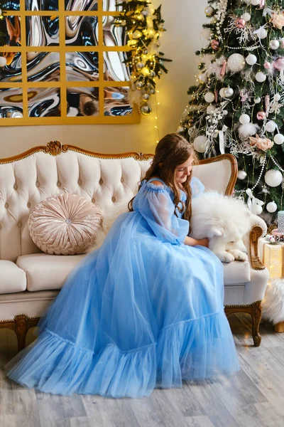 Nice girl in a light blue dress with white Samoyed dog in the studio in the New Year decorations, against the background of the Christmas tree looking at window and dreaming