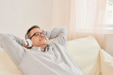 Elderly man in headphones enjoying while listening to music. Senior resting in comfortable leisure setting, enjoying the serenity of healthy aging and retirement. Recreation, lifestyle, happiness