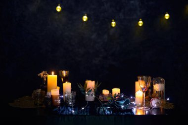 Karanlık bir restoranda romantik bir gece sahnesi dekorasyonlu bir masa seti, parlayan mumlar ve bir dizi buzlu ışıkla aydınlatılmış kırmızı şarap kadehleri.