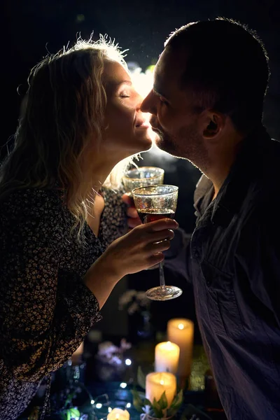 stock image A romantic close-up of an elegant couple holding wine glasses, illuminated with moody backlight and smoke, with candles on the table creating an intimate atmosphere.