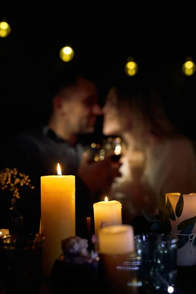 Romantic Night Date in Restaurant with Wine and Candles. Back view of couple embracing at a decorated table with burning candles and glasses of red wine.