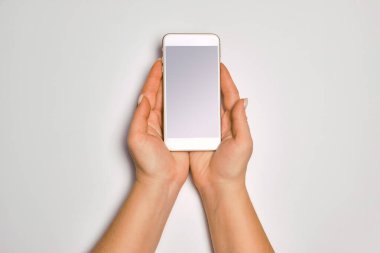 Modern cep telefonunu tutan kadın elleri. Kadın ellerinin boş ekranlı akıllı telefonu tutmasına yakın çekim. Uygulamanızın beyaz arkaplana izole edilmesi için boş akıllı telefon beyaz ekranı hazır.