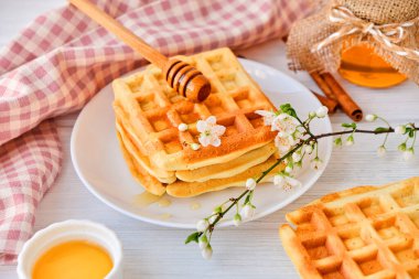 Taze Belçika waffle 'larının üzerine bal dökülüyor. Mineral ve vitamin açısından zengin organik sağlıklı bahar kahvaltısı. Kahvaltı için eko-yemek. Kiraz çiçekleriyle moda tatlı şekerlemeler