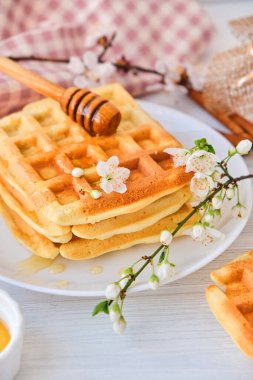 Taze Belçika waffle 'larının üzerine bal dökülüyor. Mineral ve vitamin açısından zengin organik sağlıklı bahar kahvaltısı. Kahvaltı için eko-yemek. Kiraz çiçekleriyle moda tatlı şekerlemeler