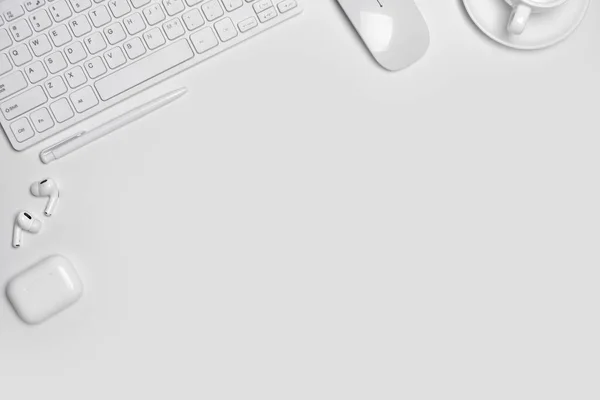 Total white workplace table with mouse, keyboard, headphones on white background with copy space.