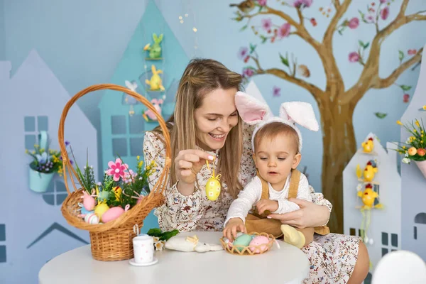 Happy holiday. Mother and her daughter with painting eggs. Family celebrating Easter. Cute little child girl is wearing bunny ears.